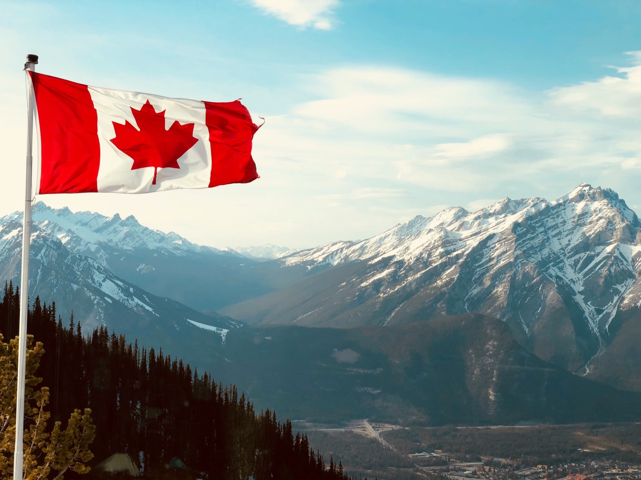 Drapeau canadien flottant devant des montagnes enneigées sous un ciel clair